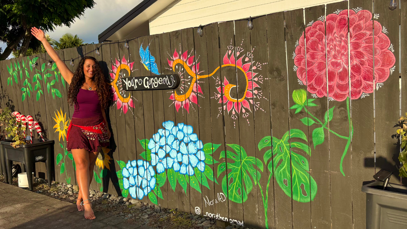 Nora standing in front of her hand-painted botanical fence mural