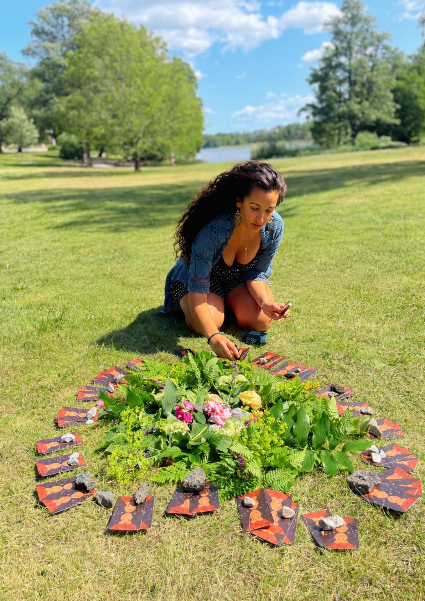 Nora arranging flowers and art cards in a circle on a sunny lawn in Stockholm