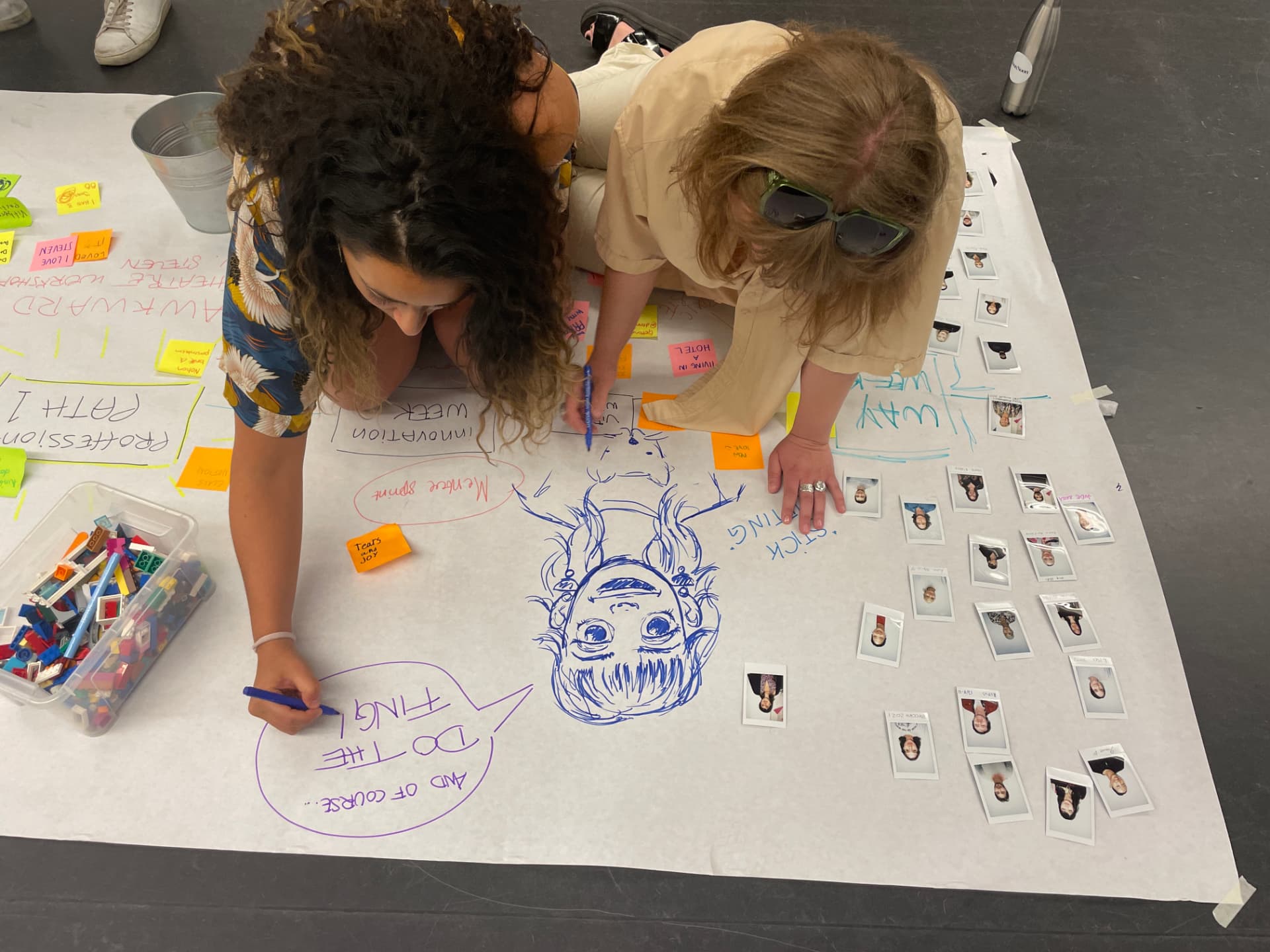 Two people collaborating on a large creative workshop drawing with markers and polaroid photos
