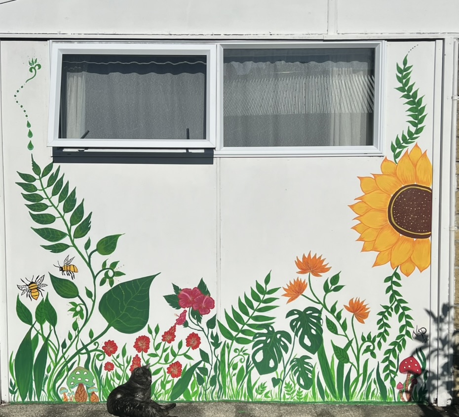 A hand-painted garden mural with sunflowers, ferns, bees and a cat on a white wall