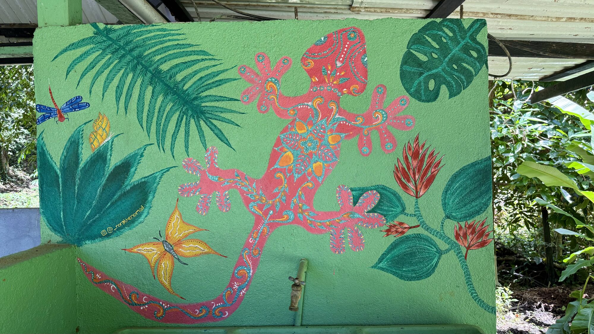 A bright pink gecko with jungle leaves and butterflies painted on a green wall