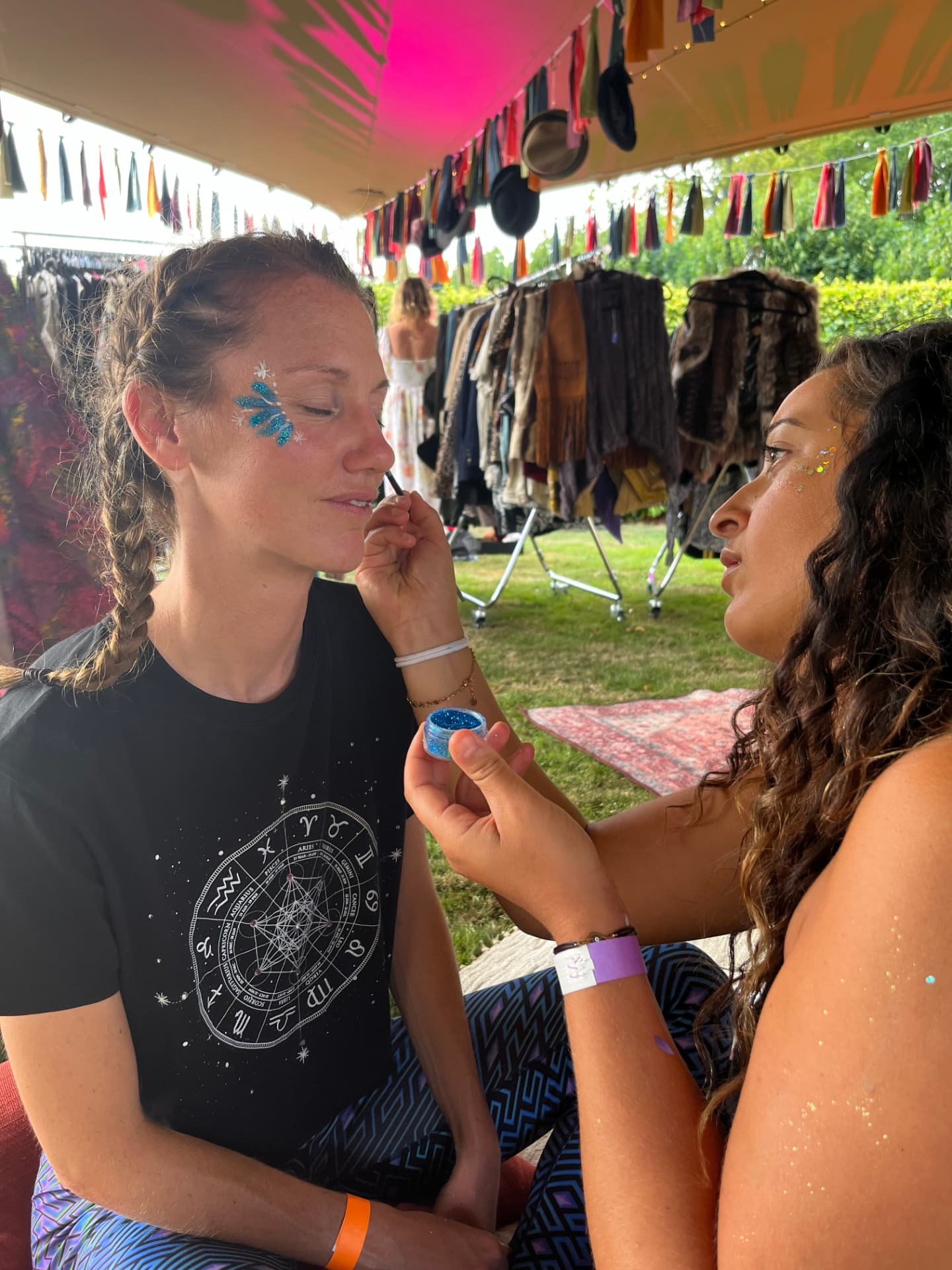 Nora applying blue glitter face paint at an outdoor festival