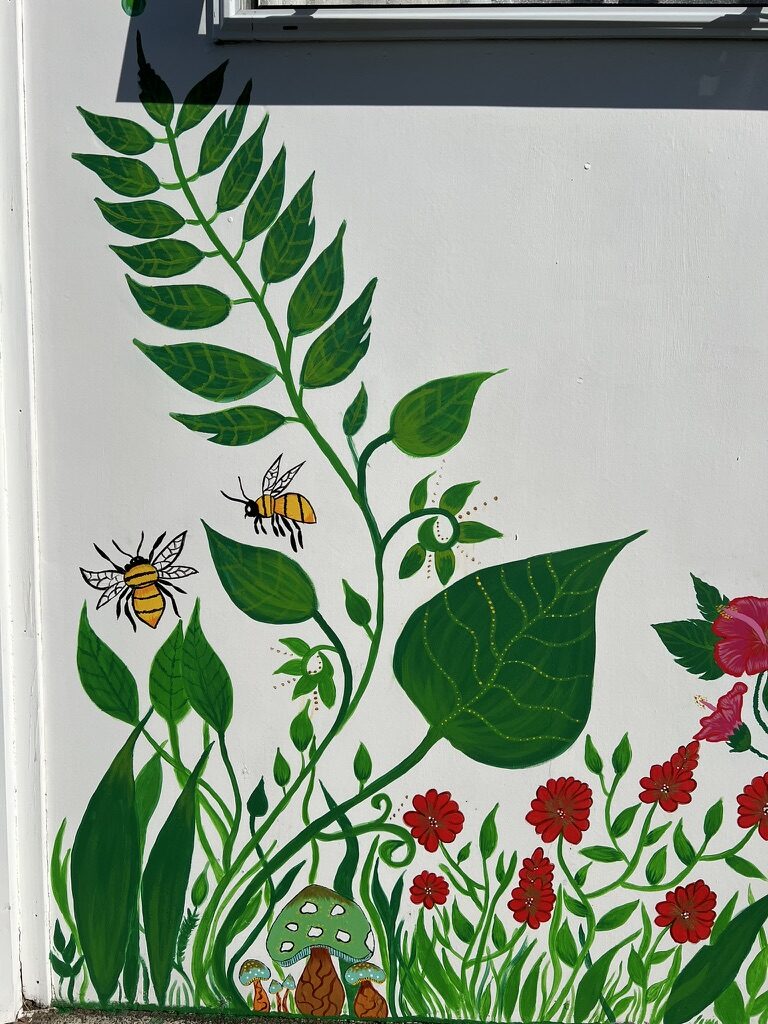 A painted garden of ferns, bees, red flowers and mushrooms climbing a white wall